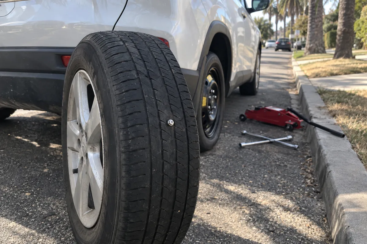 Flat tire with a screw in the tread leaning against an SUV after the spare was put on