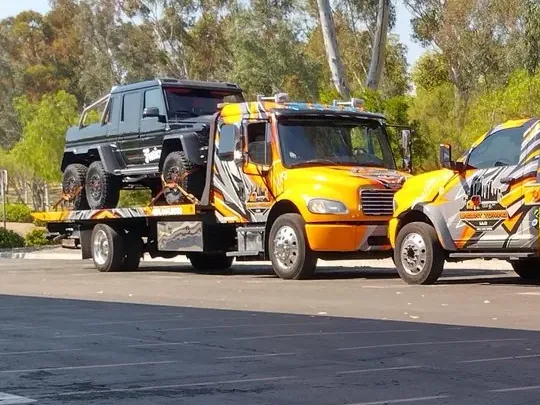 Two orange Urgent Towing flatbeds parked in a lot