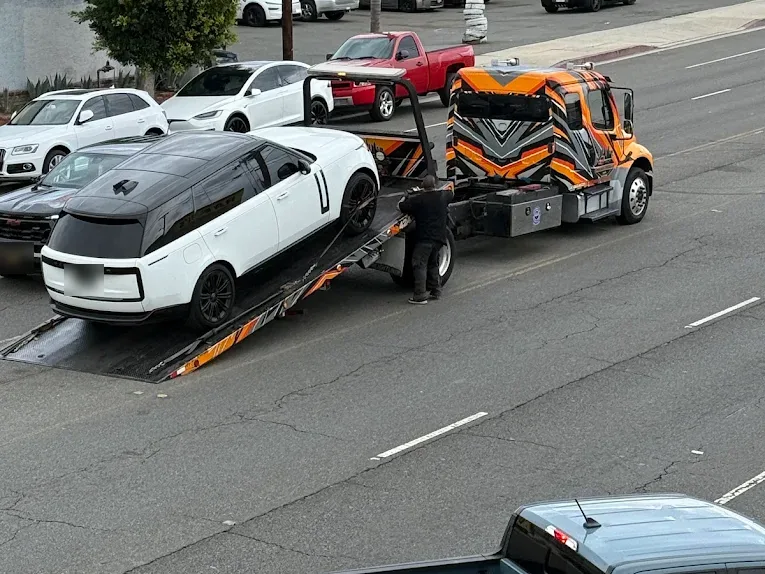 Orange Urgent Towing flatbed loading a white SUV on a city street