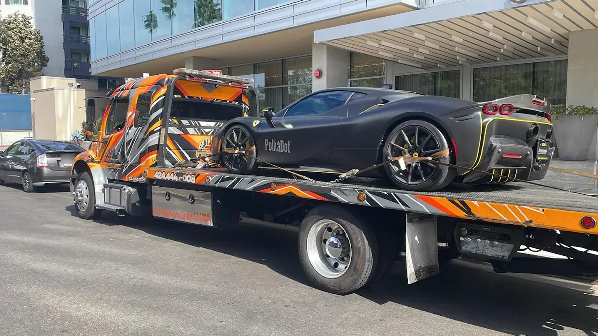 Orange Urgent Towing flatbed carrying a sports car outside a glass office building