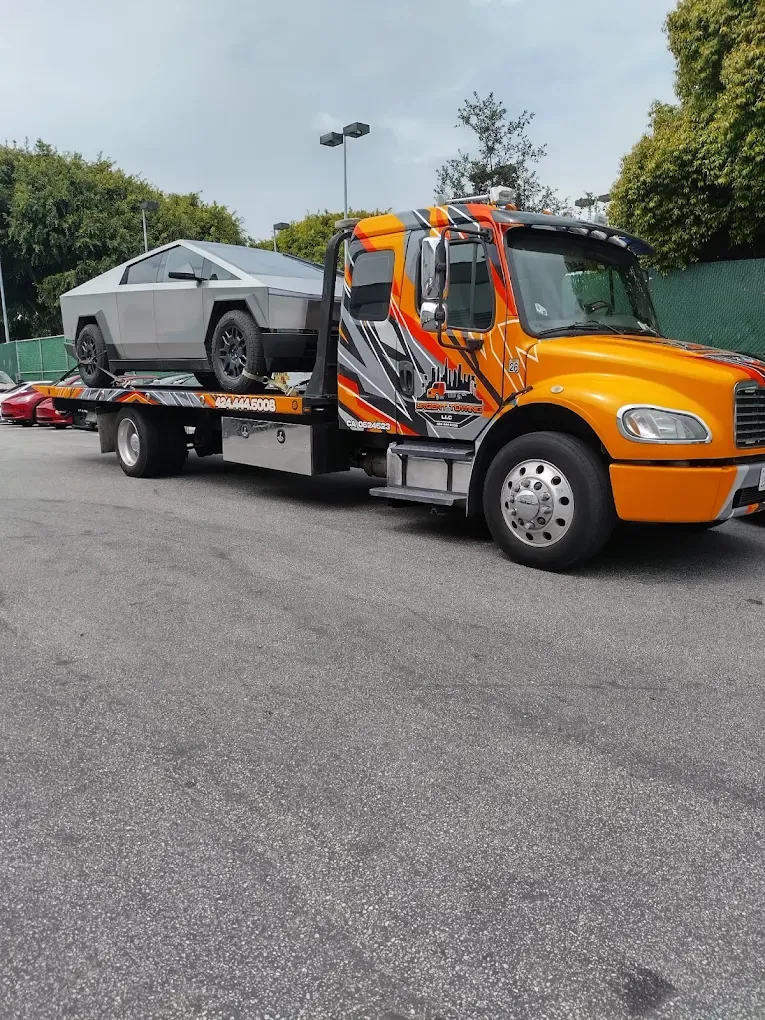 Orange Urgent Towing flatbed carrying a Tesla Cybertruck