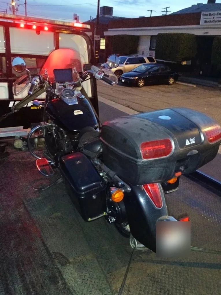 Black touring motorcycle strapped down on an Urgent Towing flatbed at dusk