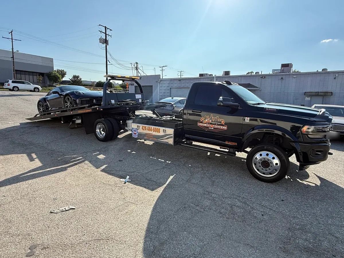 Black Urgent Towing Ram flatbed with a sports car on the bed