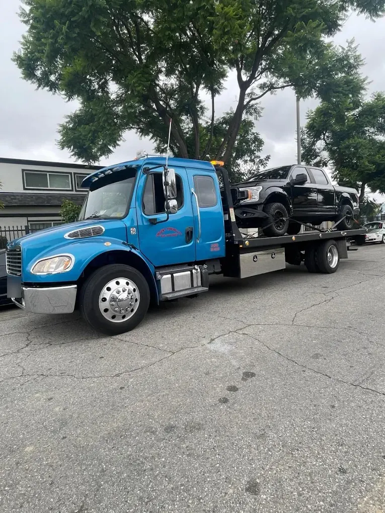 Blue Urgent Towing flatbed with a pickup truck on the bed