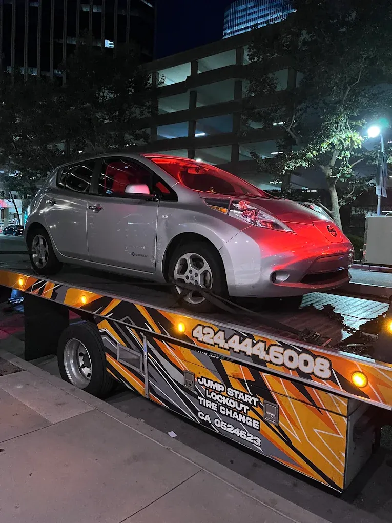 Urgent Towing flatbed at night; the side lists jump start, lockout and tire change
