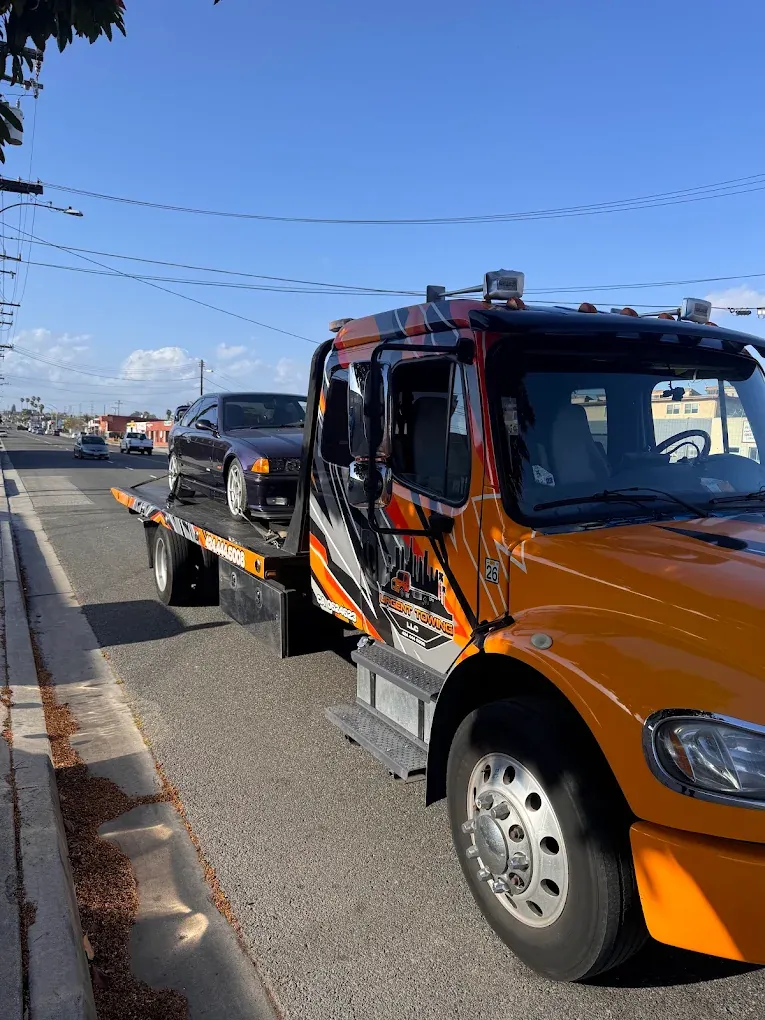 Orange Urgent Towing flatbed carrying a car on a city street