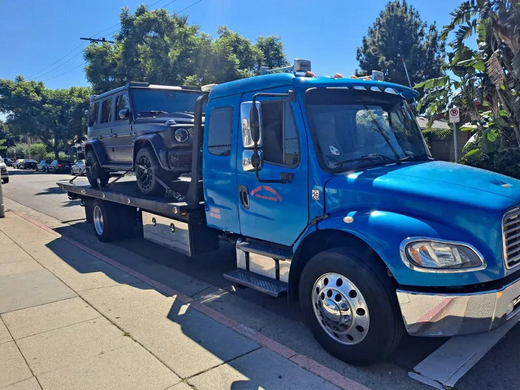 Blue Urgent Towing flatbed tow truck carrying an SUV