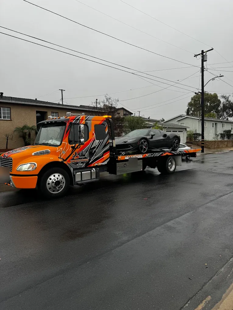 Orange Urgent Towing flatbed carrying a sports car on a residential street on a rainy day