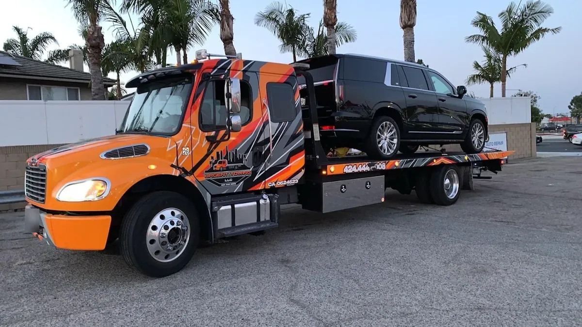 Orange Urgent Towing flatbed carrying a black SUV