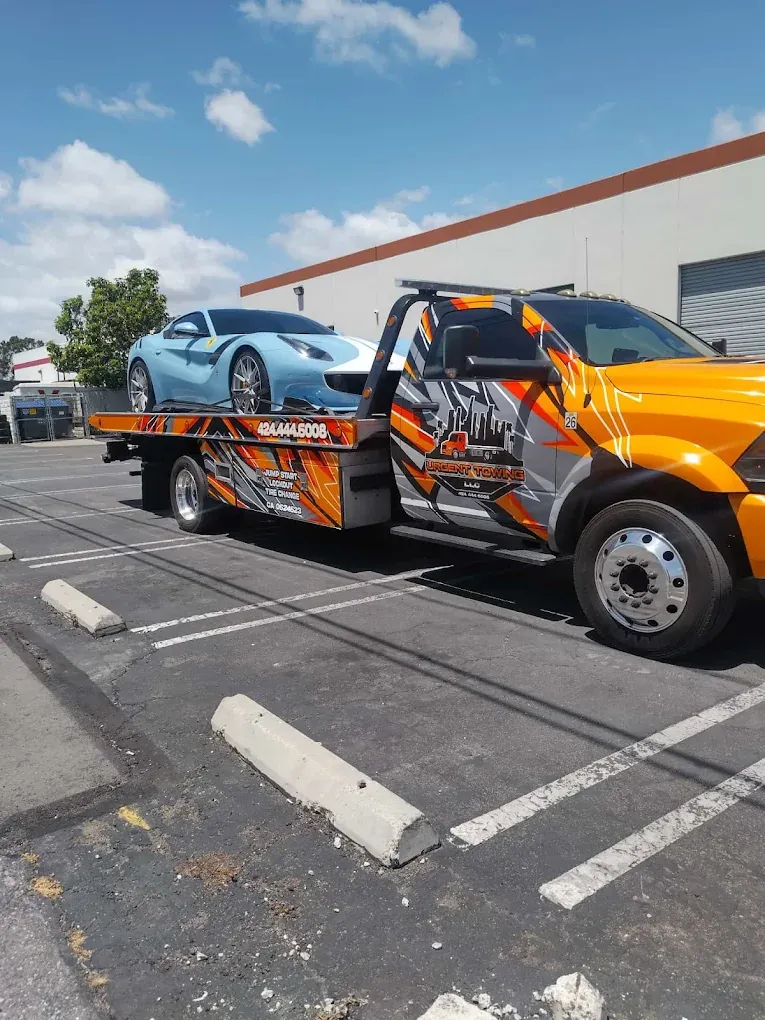 Orange Urgent Towing Ram flatbed carrying a light blue sports car
